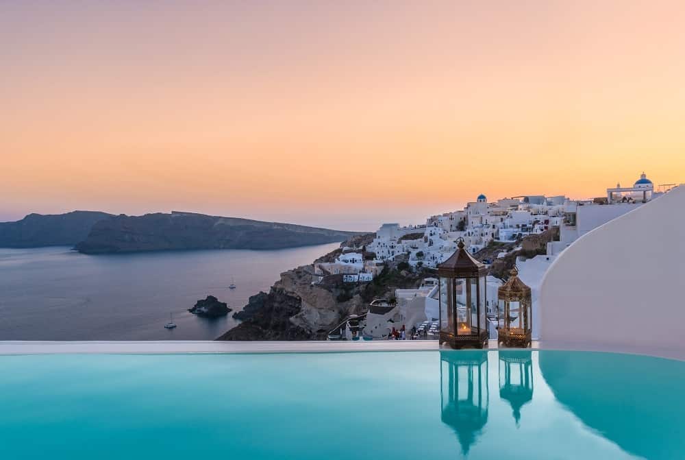 Whitewashed luxury villa with private infinity pool overlooking Santorini's caldera at sunset, featuring curved Cycladic architecture