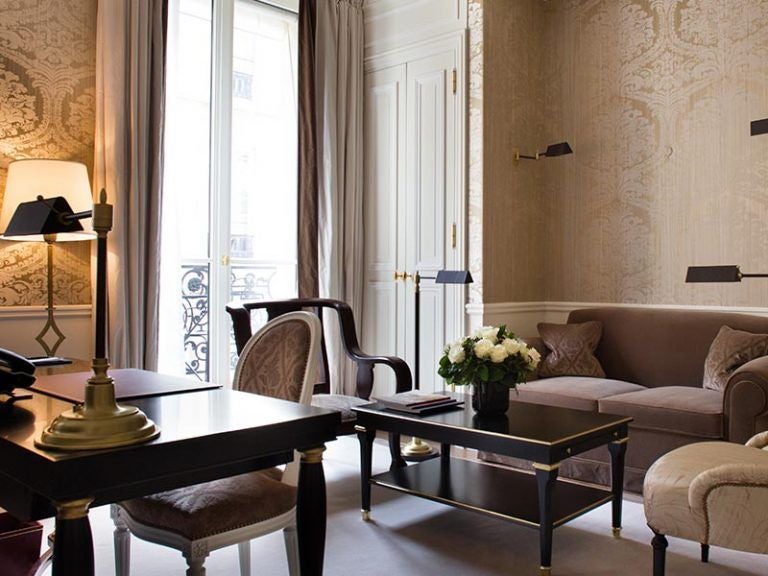 Opulent Parisian junior suite featuring silk-draped windows, antique furnishings, and a plush king bed with gold accents and damask walls