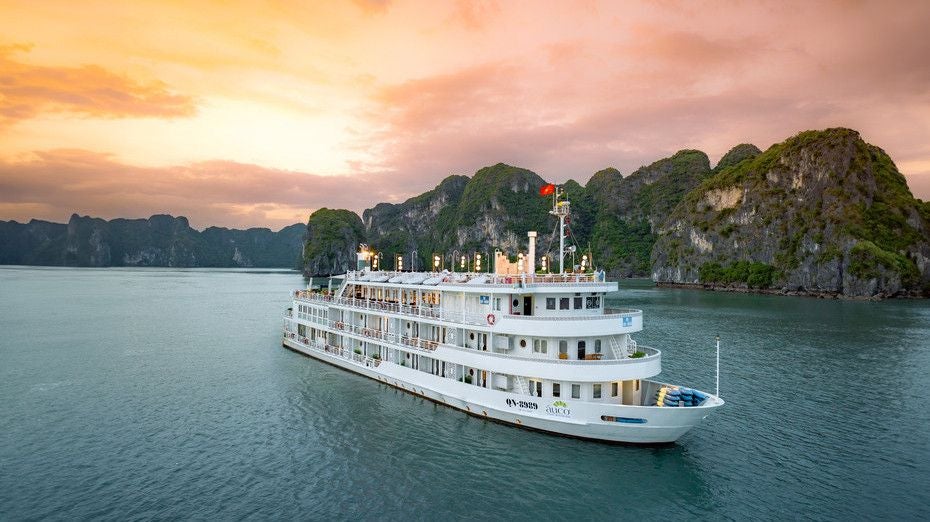 Elegant white cruise ship anchored in scenic Halong Bay, Vietnam, with limestone karsts and emerald waters in background, showcasing luxury maritime travel