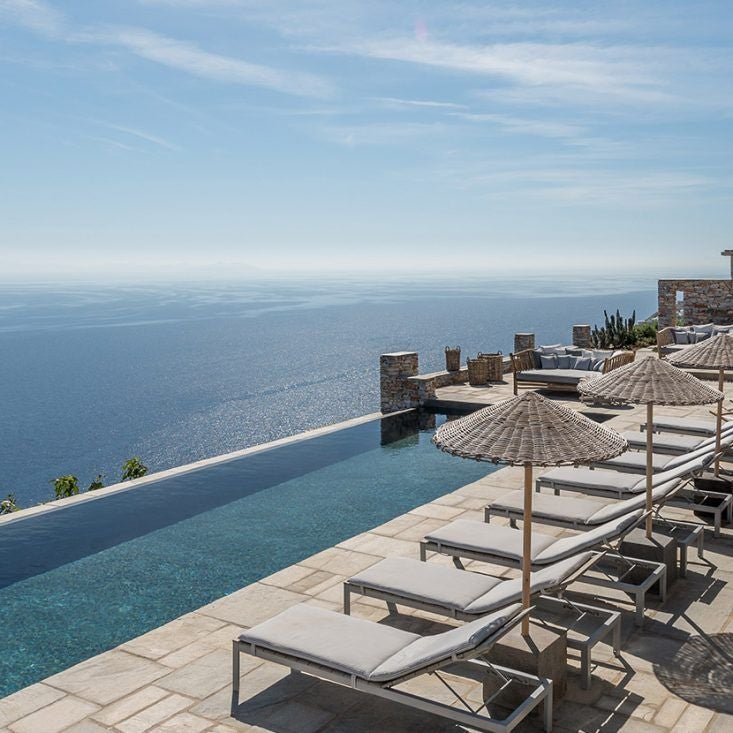 Sleek white minimalist Cycladic hotel perched on Sifnos hillside, overlooking azure Aegean Sea with elegant infinity pool at sunset