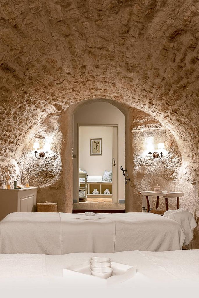 Historic luxury hotel with stone walls nestled in Provence countryside, featuring terracotta roofs and panoramic mountain views