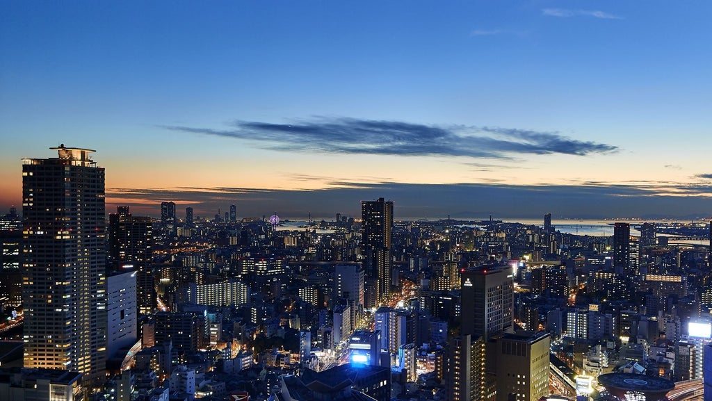 Elegant high-rise hotel facade with Art Deco details, ornate gold accents, and landscaped gardens beneath a clear blue Osaka sky