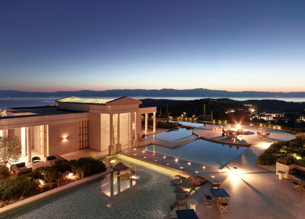 Elegant infinity pool with sun loungers overlooking the Aegean Sea at sunset, framed by sleek Grecian columns and Mediterranean foliage