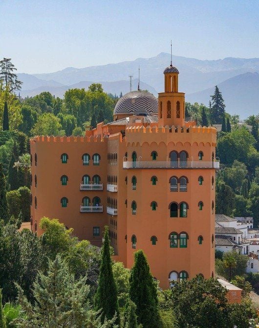 Historic luxury hotel with ornate Moorish architecture, terracotta facade and arched windows overlooking Granada's palm-lined gardens