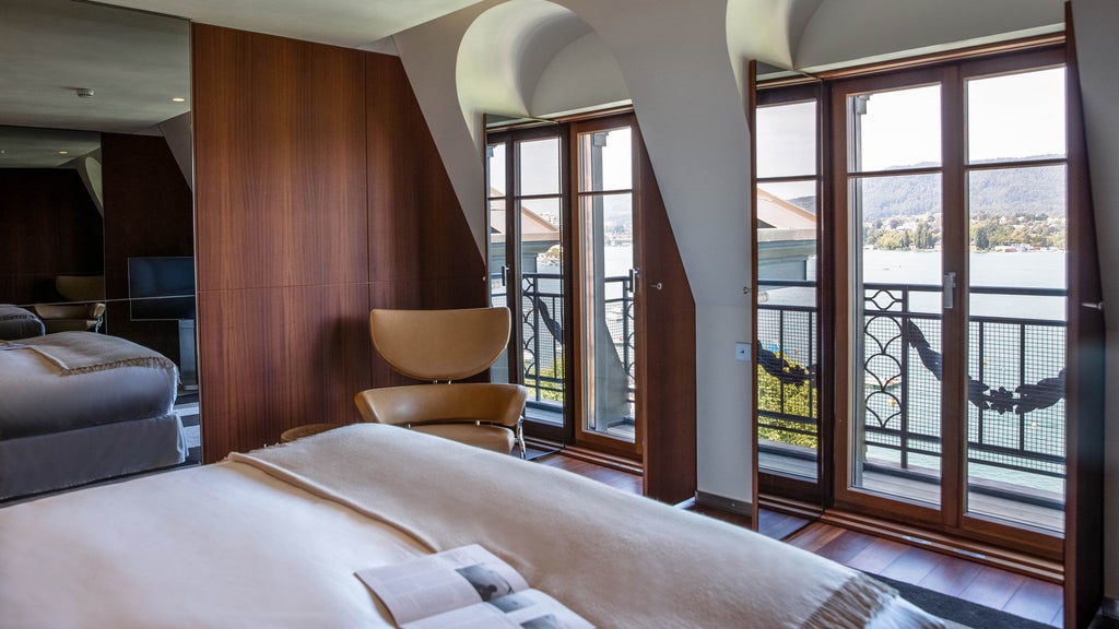 Elegant lakeside hotel in Zurich with classic belle époque facade, ornate balconies, and Swiss flags against blue sky and Lake Zurich