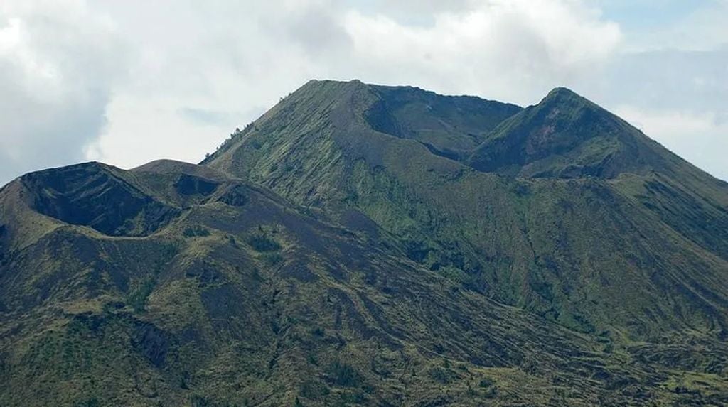 Lush green Balinese rice terraces of Jatiluwih UNESCO site with traditional trekking guide, majestic Batukaru Temple in scenic background, verdant landscape