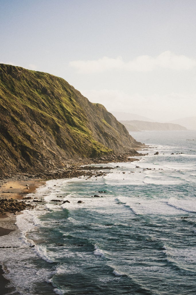 Rugged Basque coastline at sunset with dramatic cliffs meeting the Atlantic Ocean, luxury yacht marina visible in protected bay