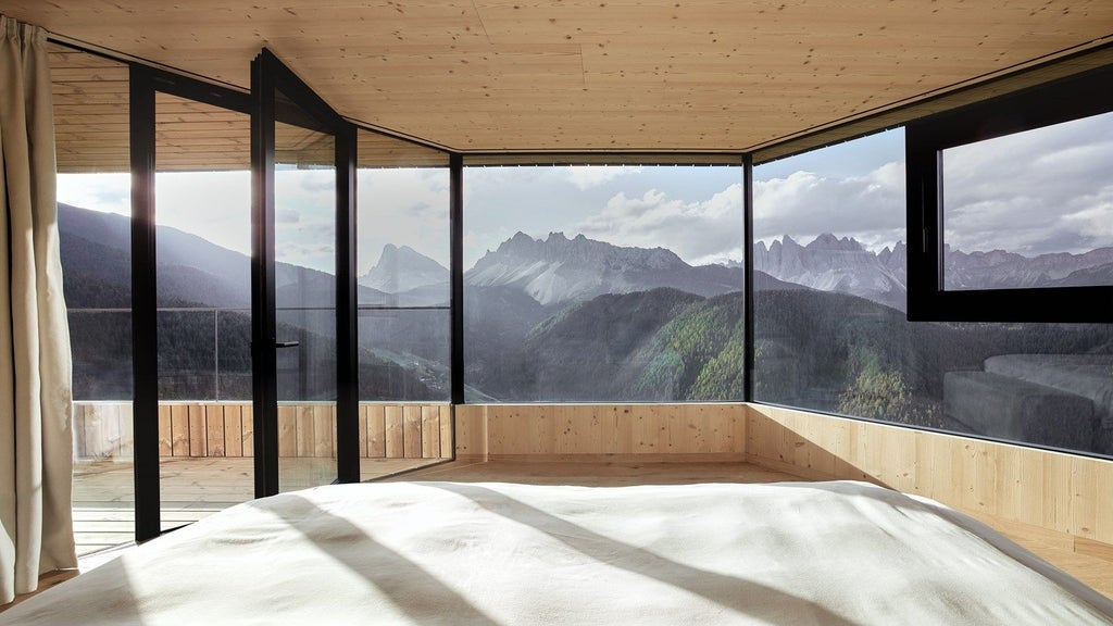 Modern luxury mountain resort with floor-to-ceiling windows reflecting snowy Dolomite peaks, featuring an infinity pool at sunset