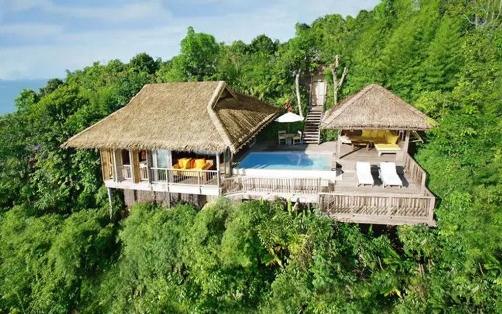 Luxurious overwater villa with infinity pool overlooking limestone karsts in Phang Nga Bay at sunset, surrounded by lush jungle