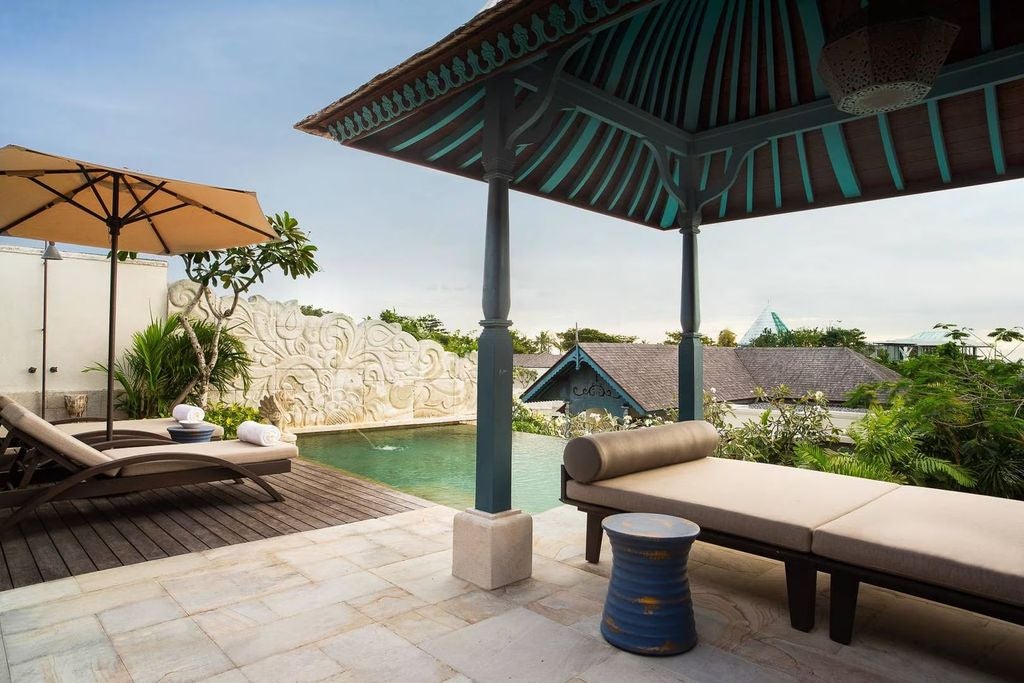 Luxurious Balinese villa bedroom with canopy bed, private pool view through floor-to-ceiling windows, and elegant wood furnishings