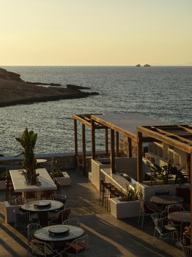 Pristine white hotel buildings with infinity pool overlooking the Aegean Sea at sunset, nestled into a Greek coastal hillside