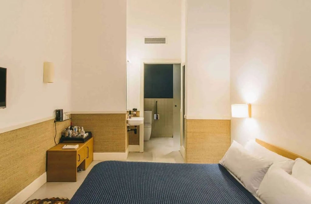 Minimalist Mediterranean hotel room with soft neutral tones, wooden furniture, crisp white linens, and large windows offering natural light in Barcelona