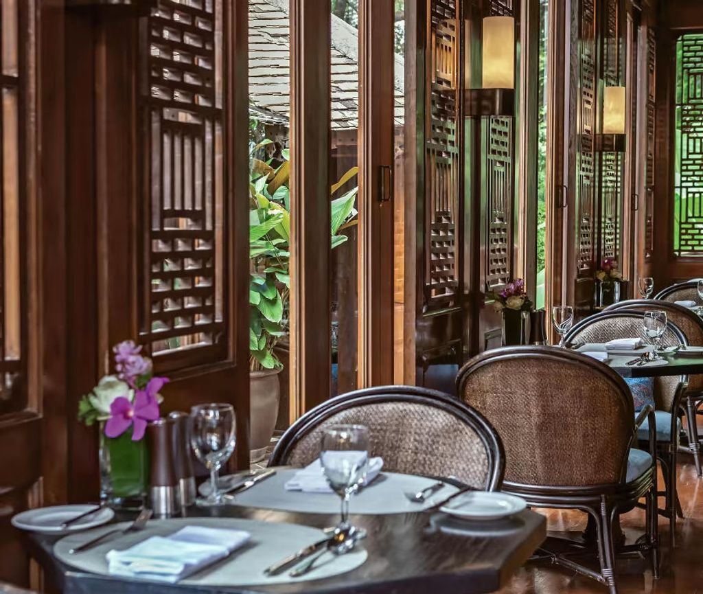 Elegant colonial-style Thai hotel with white pillars, wrap-around verandah, and tropical garden featuring mature palm trees and foliage