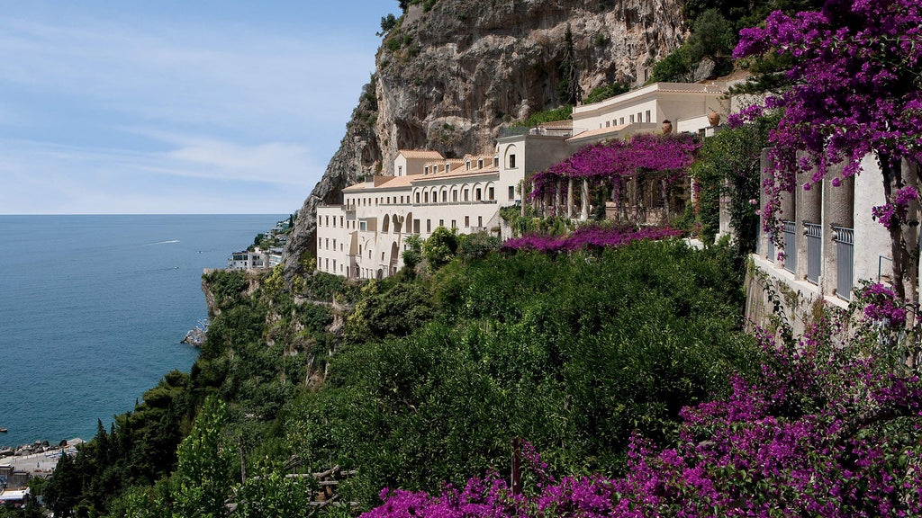 Historic Italian cliffside luxury hotel with whitewashed walls and arched terraces overlooking the Amalfi Coast's deep blue Mediterranean waters