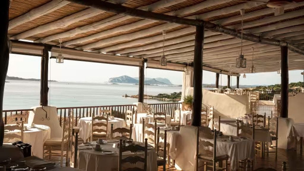 Elegant Mediterranean hotel with white-washed walls nestled on Costa Smeralda's coastline, featuring a panoramic seaside terrace and lush gardens