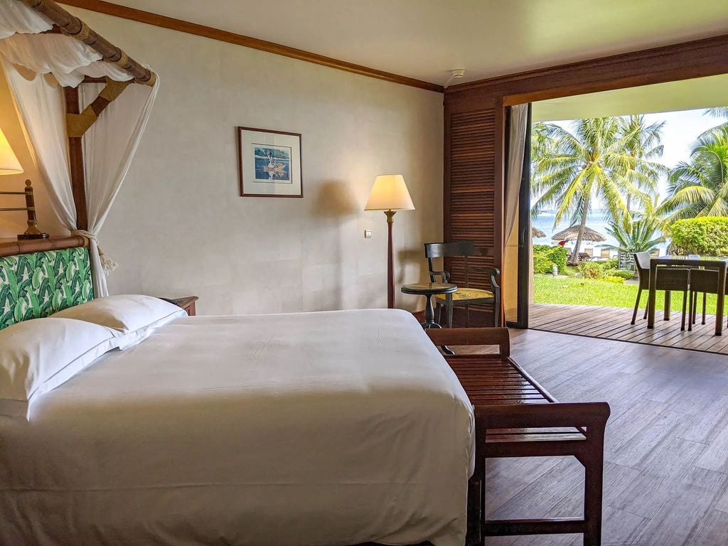 Luxurious oceanfront premium room with king bed, private balcony, traditional Polynesian decor, and panoramic lagoon views at sunset