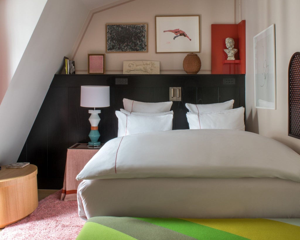 Luxurious Parisian hotel room with plush dark gray velvet headboard, crisp white linens, and moody atmospheric lighting creating elegant boutique ambiance