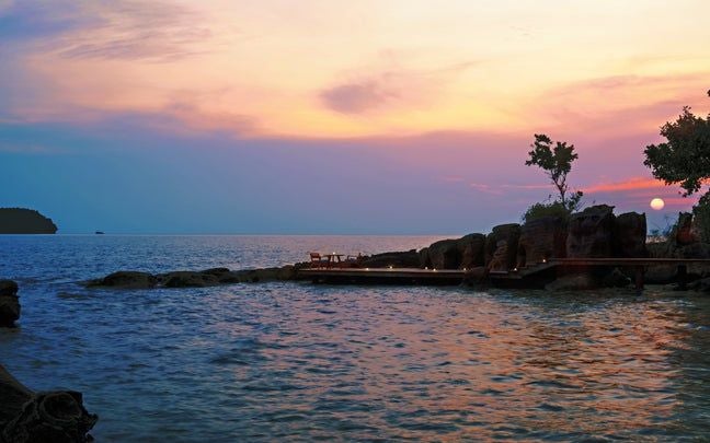 Luxurious oceanfront villa with infinity pool overlooking turquoise waters, surrounded by lush tropical gardens at sunset in Cambodia