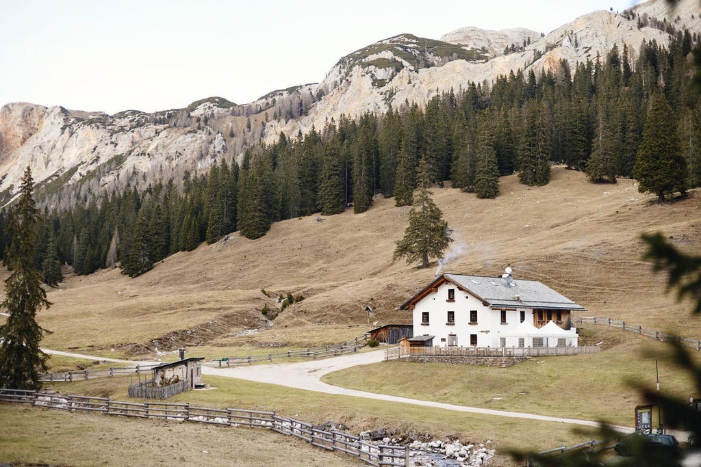 Traditional alpine lodge Malga Ra Stua nestled in snow-capped Dolomites mountains, featuring wooden balconies and window boxes with red flowers