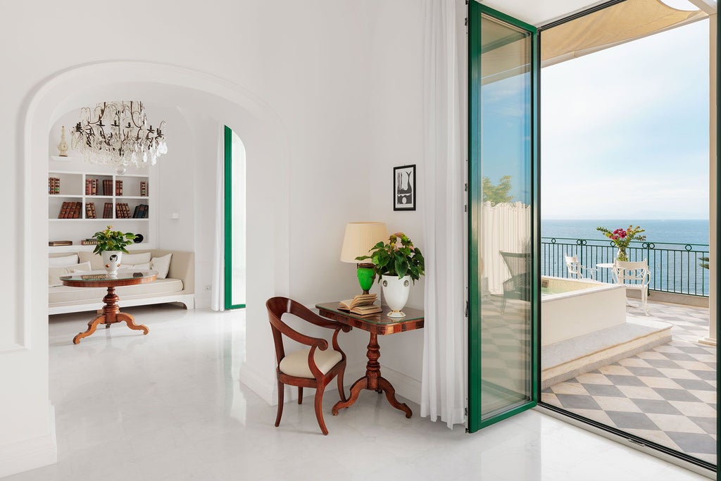 Luxurious suite overlooking Sorrento's coastline, featuring elegant marble floors, antique furnishings, and expansive sea views through floor-to-ceiling windows