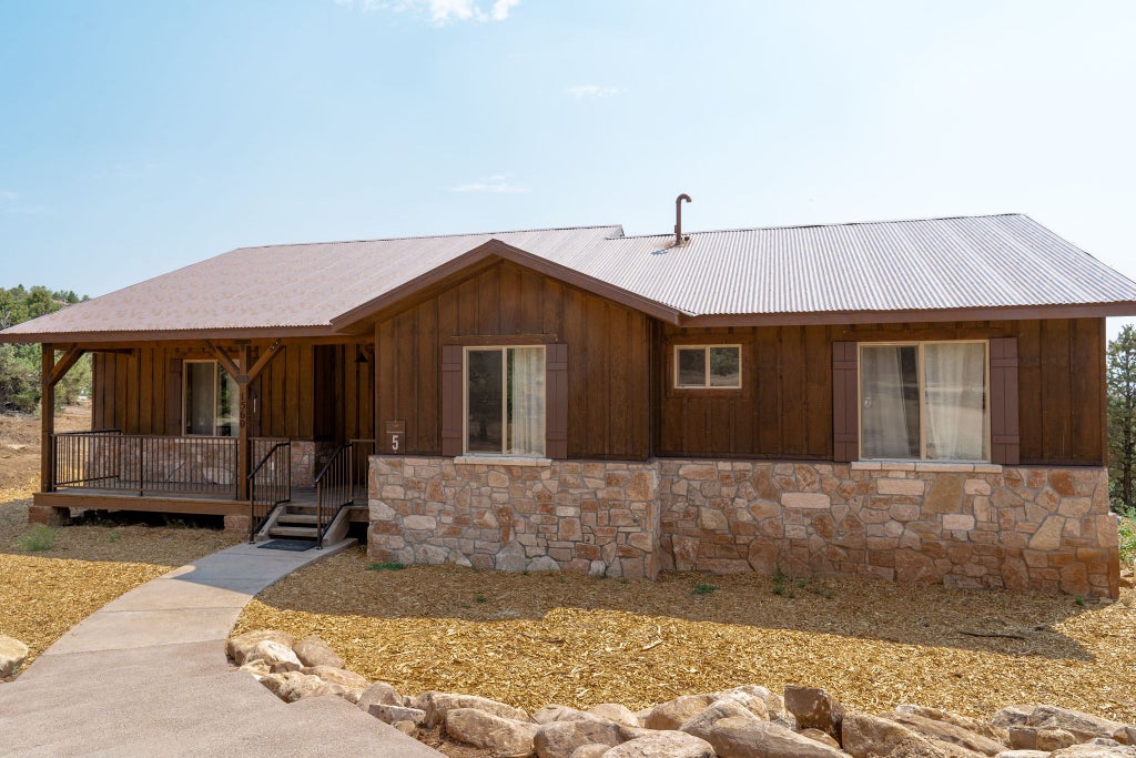 Rustic wooden lodge room with plush king bed, panoramic mountain views, elegant western decor, warm neutral tones, and large windows overlooking scenic landscape