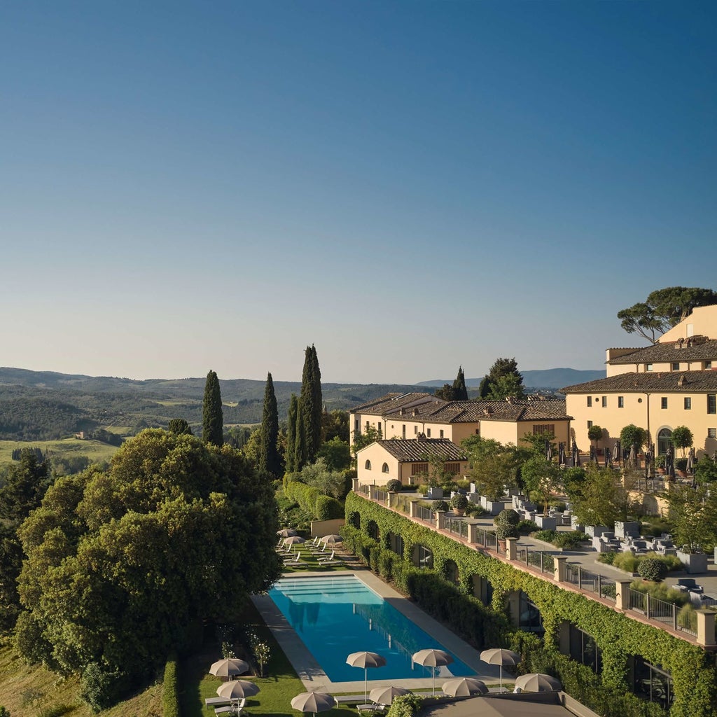 Tuscan castle-hotel with elegant stone facade set amid rolling vineyards, featuring medieval towers and manicured Italian gardens