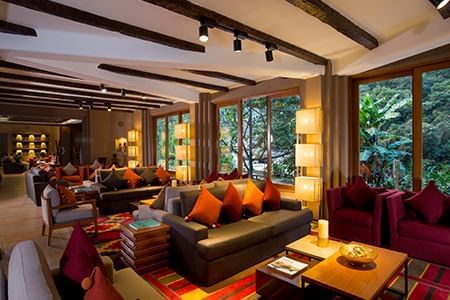 View of SUMAQ luxury hotel's stone and wood facade nestled against misty Andean mountains, with lush gardens and elegant entrance