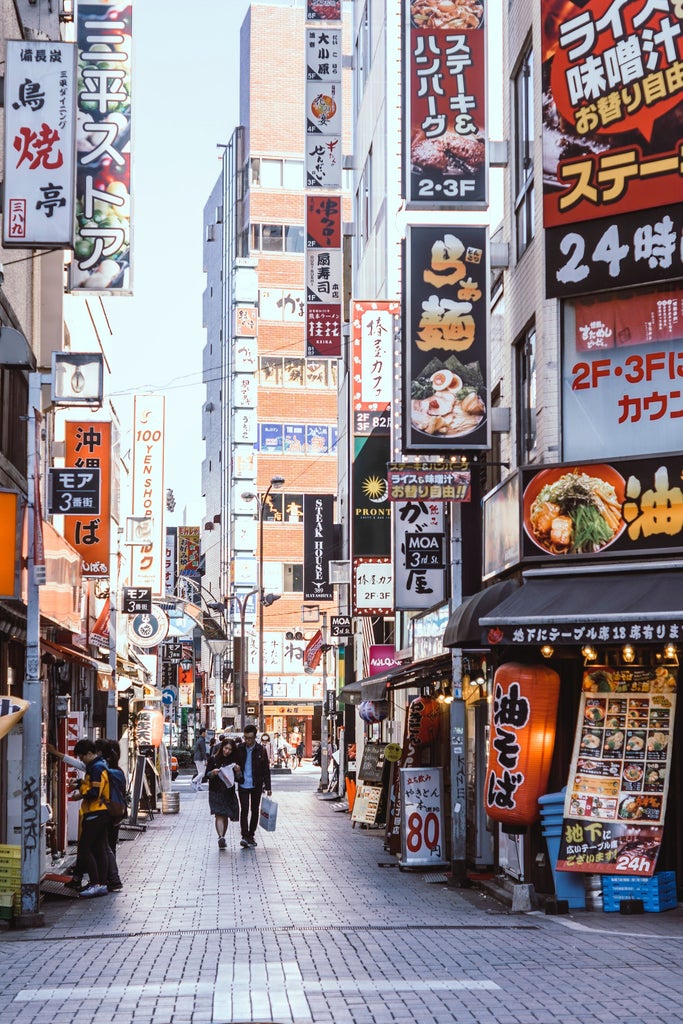 Vibrant Takeshita Street in Harajuku lined with colorful fashion boutiques, neon signs, and crowds beneath pink umbrellas