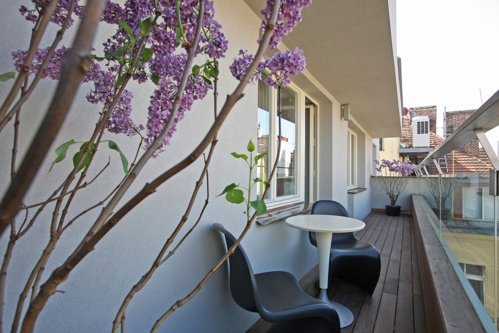 Luxurious hotel suite terrace overlooking Prague's historic cityscape, featuring modern furnishings, elegant seating, and expansive urban views at sunset