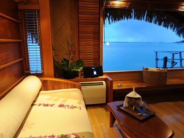 Luxurious overwater villa with private deck overlooking turquoise Polynesian lagoon, thatched roof, and direct ocean access at sunset