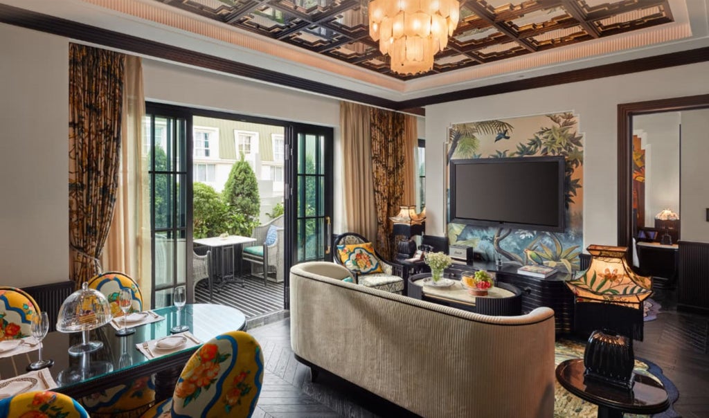 Opulent hotel suite with draped canopy bed, crystal chandelier, gold accents, and floor-to-ceiling windows overlooking Hanoi cityscape