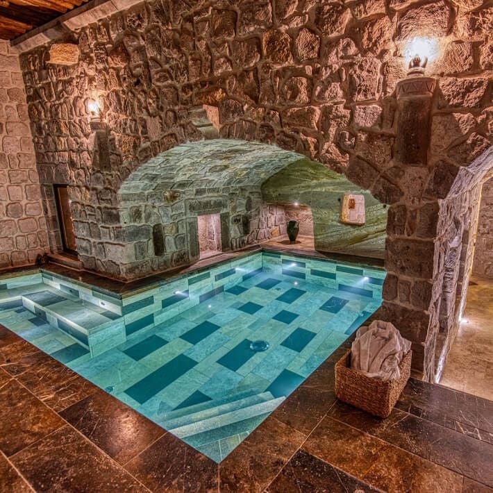 Elegant marble-clad luxury suite with panoramic windows overlooking a serene blue pool and Mediterranean landscape at Museum Hotel in Cappadocia, Turkey.