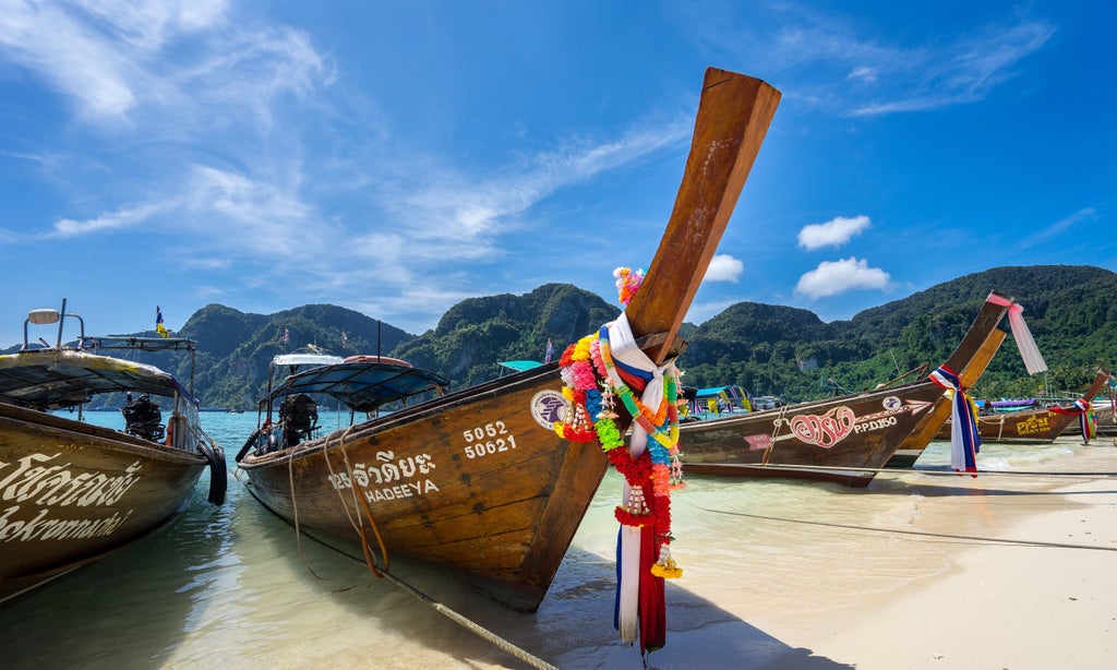 Traditional wooden long-tail boat gliding through crystal-clear turquoise waters, surrounded by limestone cliffs and pristine beaches of Thailand