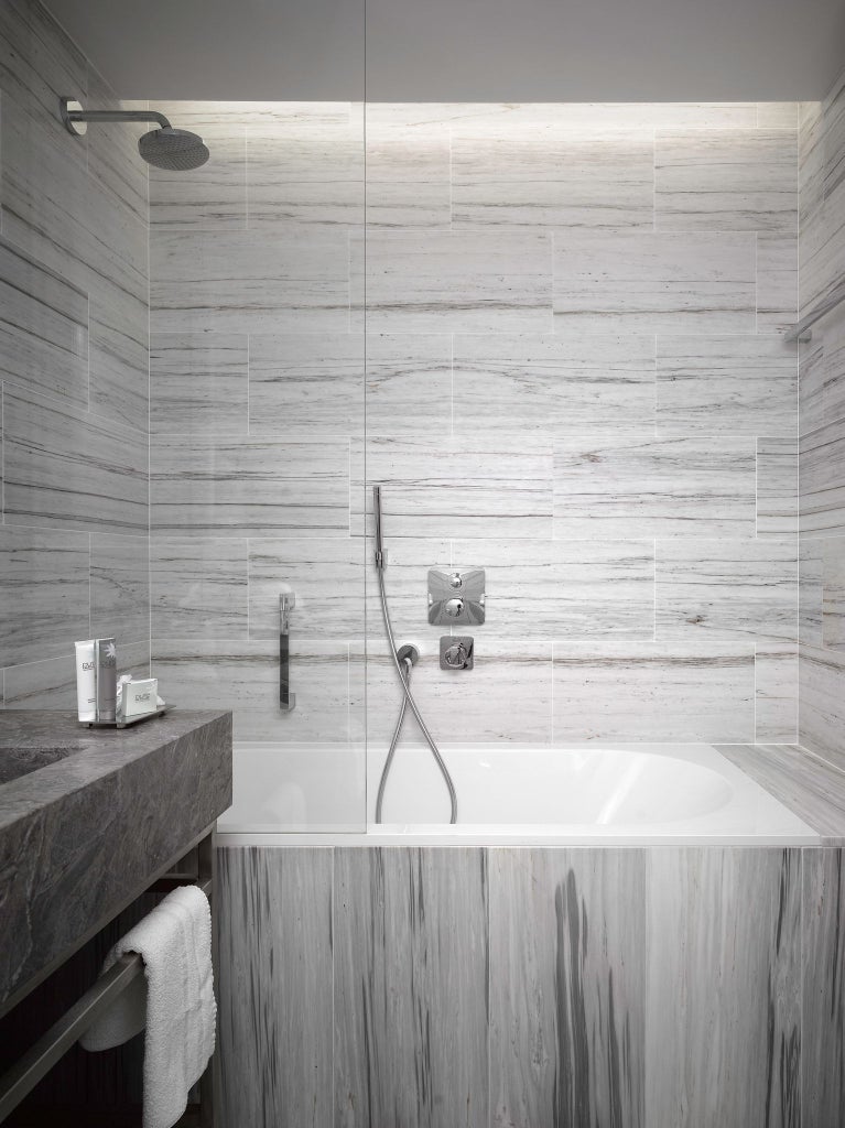 Elegant queen bedroom in scenset hotel with plush white bedding, dark wood accents, modern chandelier, and large city-view window overlooking Prague