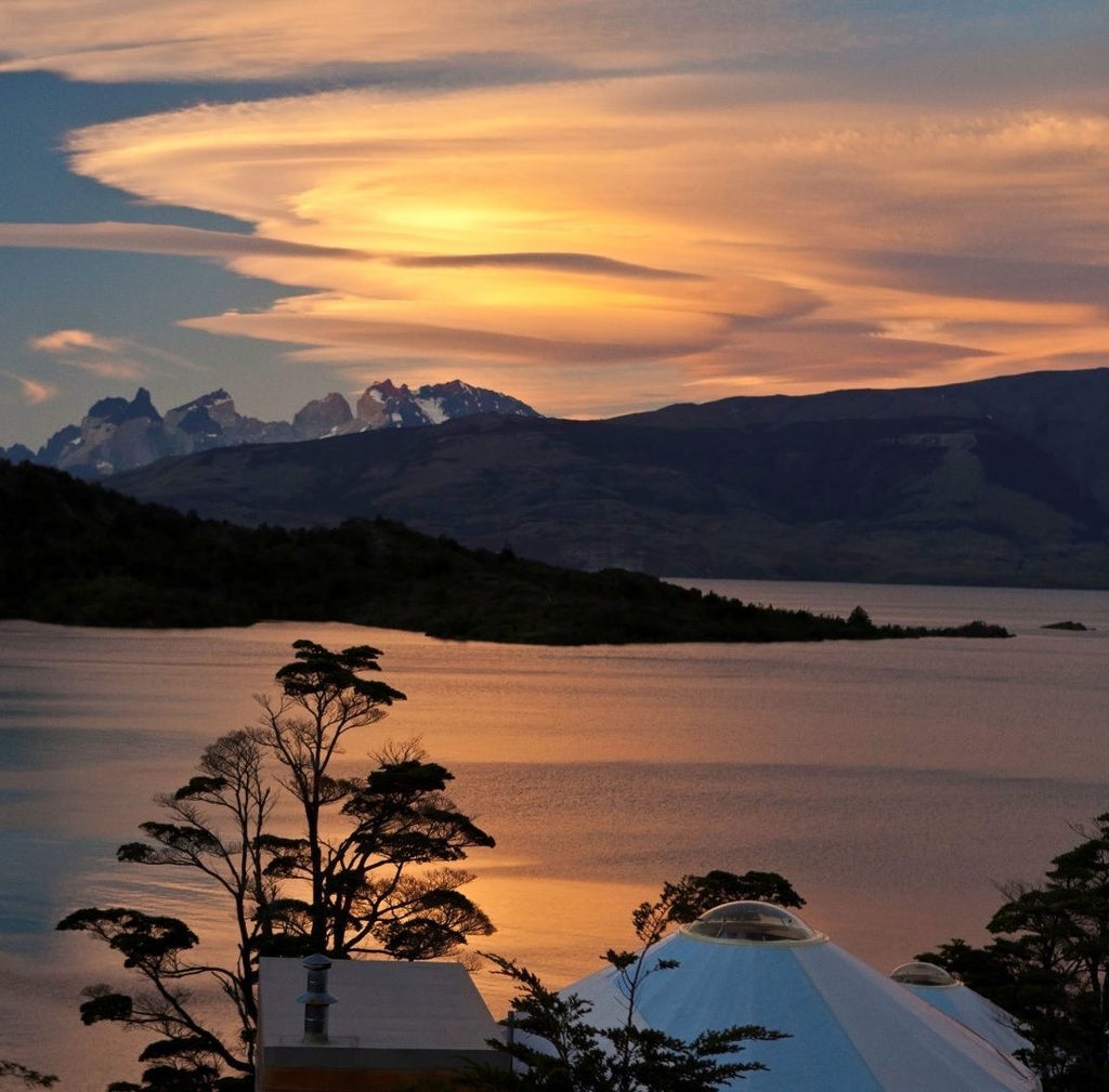 Luxury geodesic dome cabin perched on stilts amid lush Patagonian forest, overlooking serene lake and snow-capped mountain peaks