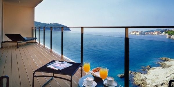 Modern luxury hotel suite with sea-facing balcony, featuring minimalist white decor, king bed, and stunning Adriatic coastline views of Dubrovnik