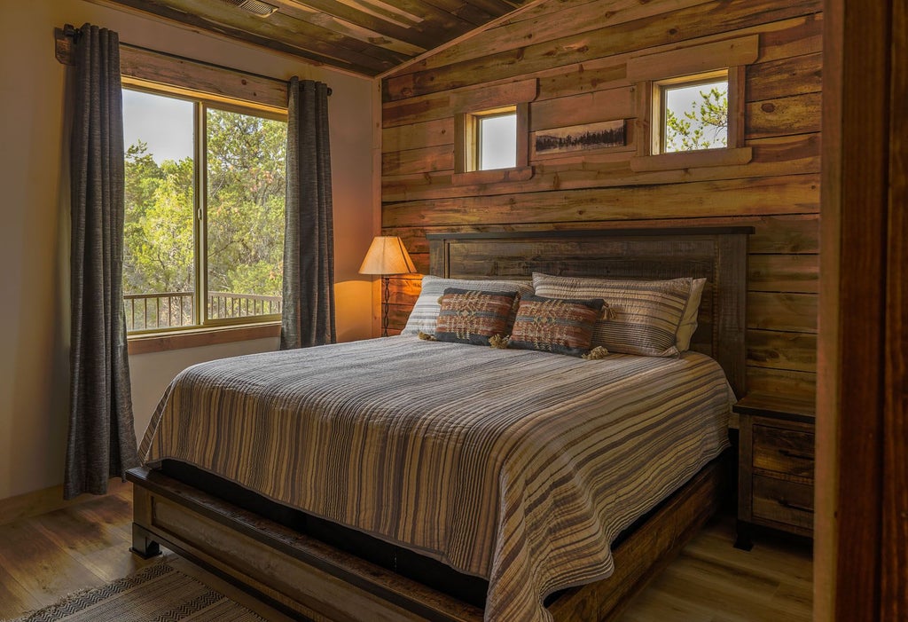 Rustic lodge bedroom with wooden furnishings, plush bedding, and large windows overlooking scenic mountain landscape at Scenset Mountain Ranch