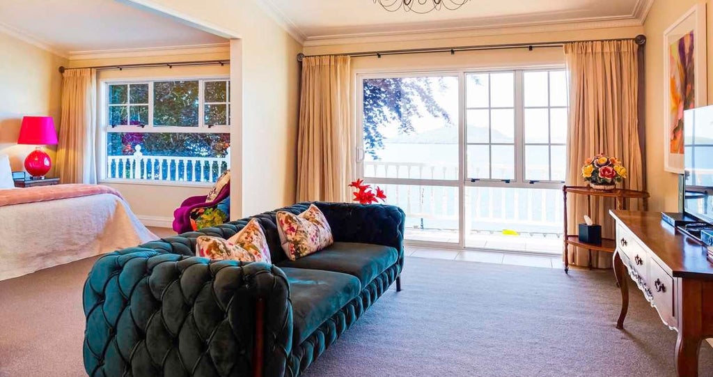 Luxurious lodge suite with panoramic views of rugged New Zealand landscape, featuring elegant wooden furnishings and floor-to-ceiling windows overlooking scenic terrain.