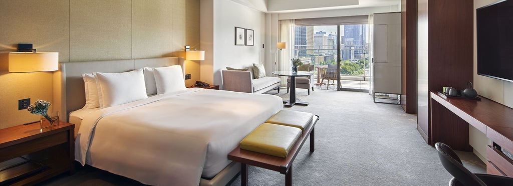 Elegant hotel room with modern Japanese design, featuring plush king bed, floor-to-ceiling windows overlooking Wadakura Fountain Park in Tokyo