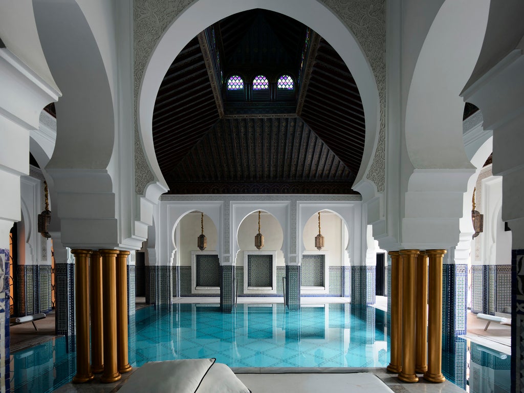 Ornate Moroccan archways frame a luxurious hotel courtyard with traditional tilework, flowing fountains and manicured gardens at La Mamounia