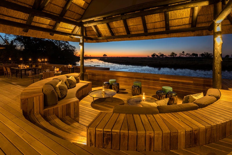 Luxurious safari lodge deck overlooking African savanna, with plush lounge chairs and private plunge pool at sunset