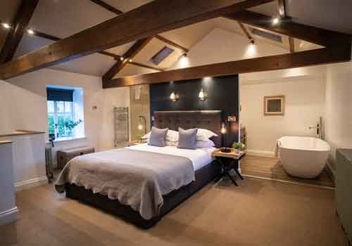 Luxurious barn suite with neutral color palette, king-sized bed, exposed wooden beams, contemporary decor, and panoramic countryside view at boutique UK hotel