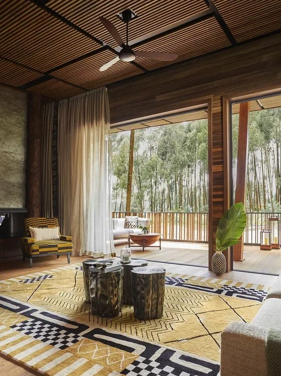 Luxurious Rwandan suite with modern African design, volcanic stone walls, floor-to-ceiling windows overlooking lush rainforest landscape near mountain gorilla habitat