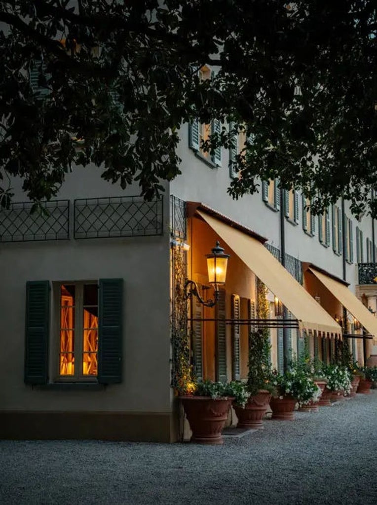 Elegant Italian villa with cream facade and ornate balconies overlooks Lake Como, surrounded by manicured gardens and cypress trees