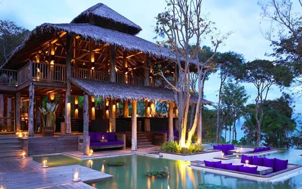 Luxurious infinity pool overlooking limestone cliffs and turquoise Phang Nga Bay waters, with tropical foliage and wooden sun deck