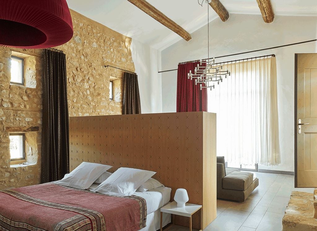 Elegant stone-walled French suite with plush white bedding, soft natural light, and rustic chic decor in a historic Provençal boutique hotel bedroom