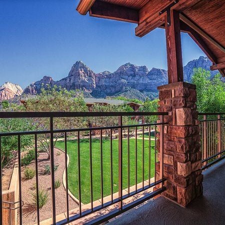 Luxurious mountain lodge exterior with stone facade, expansive windows, and wooden beams nestled against dramatic red rock cliffs