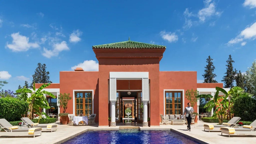 Luxurious Moorish-style resort nestled in a lush garden, with elegant white architecture, reflecting pools, and distant Atlas Mountains in Morocco.