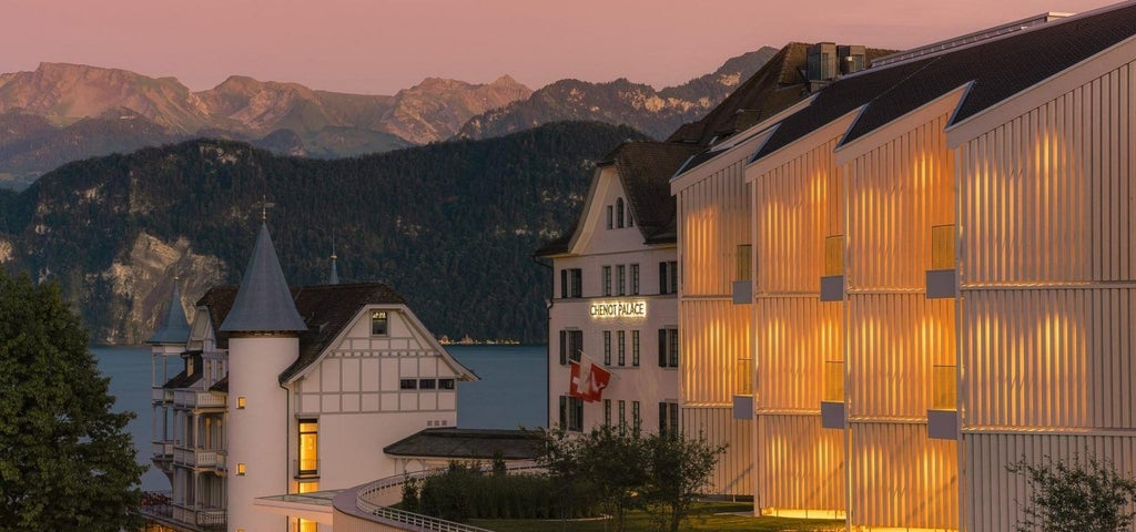 Luxury lakeside wellness hotel with modern glass facade nestled between Swiss Alps and Lake Lucerne, surrounded by manicured gardens