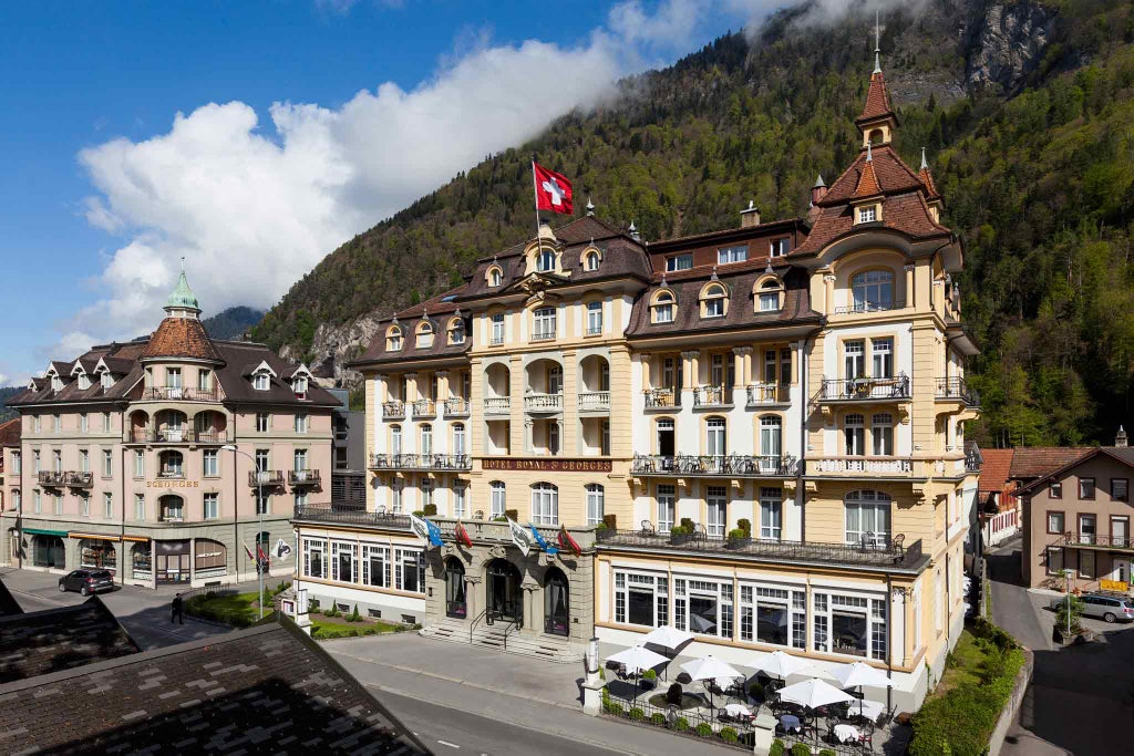 Elegant white baroque-style luxury hotel with ornate balconies and classic window arches set against Swiss Alps backdrop in Interlaken